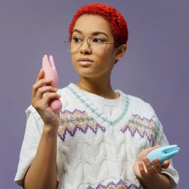 woman with red hair holding pink and teal vibrators